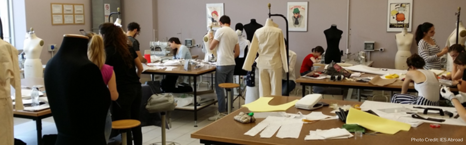 Students mill about a classroom with many mannequins wearing different styles of  black and white clothes. 